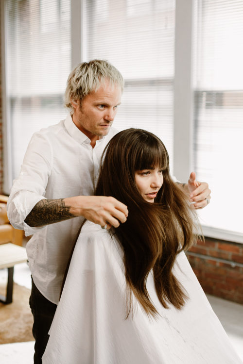 A hair stylist styles his client's bangs.