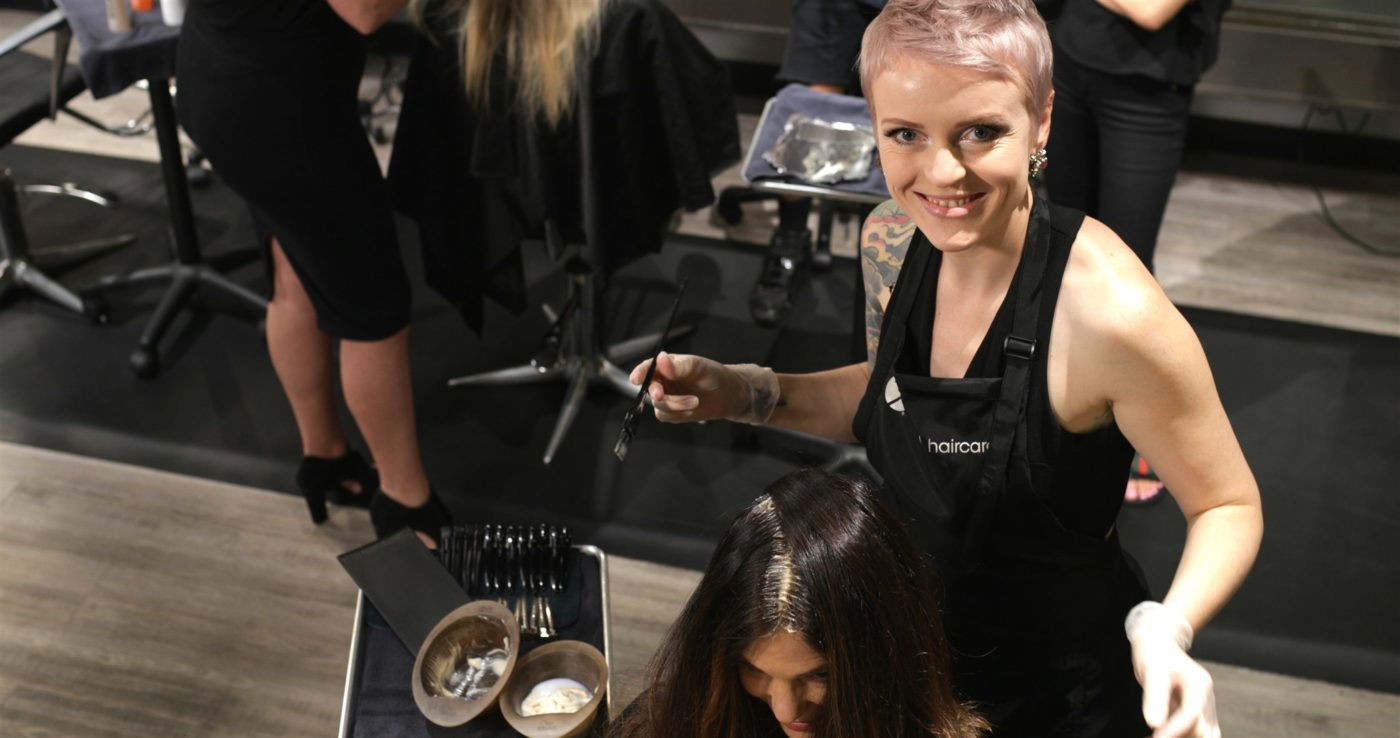 A hairstylist looks up from her client and smiles.