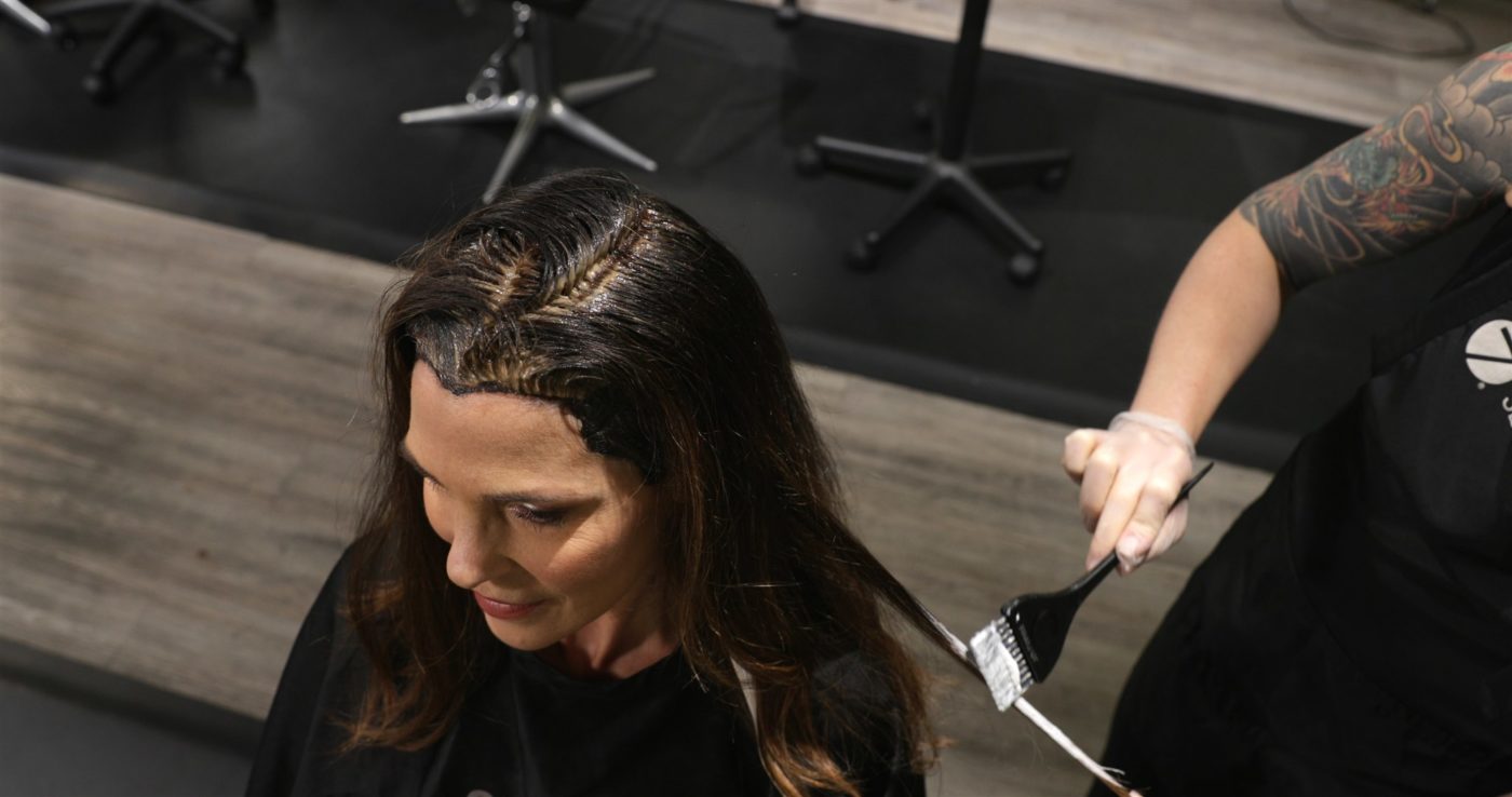 A hairstylist covers the ends of her client's  long hair.