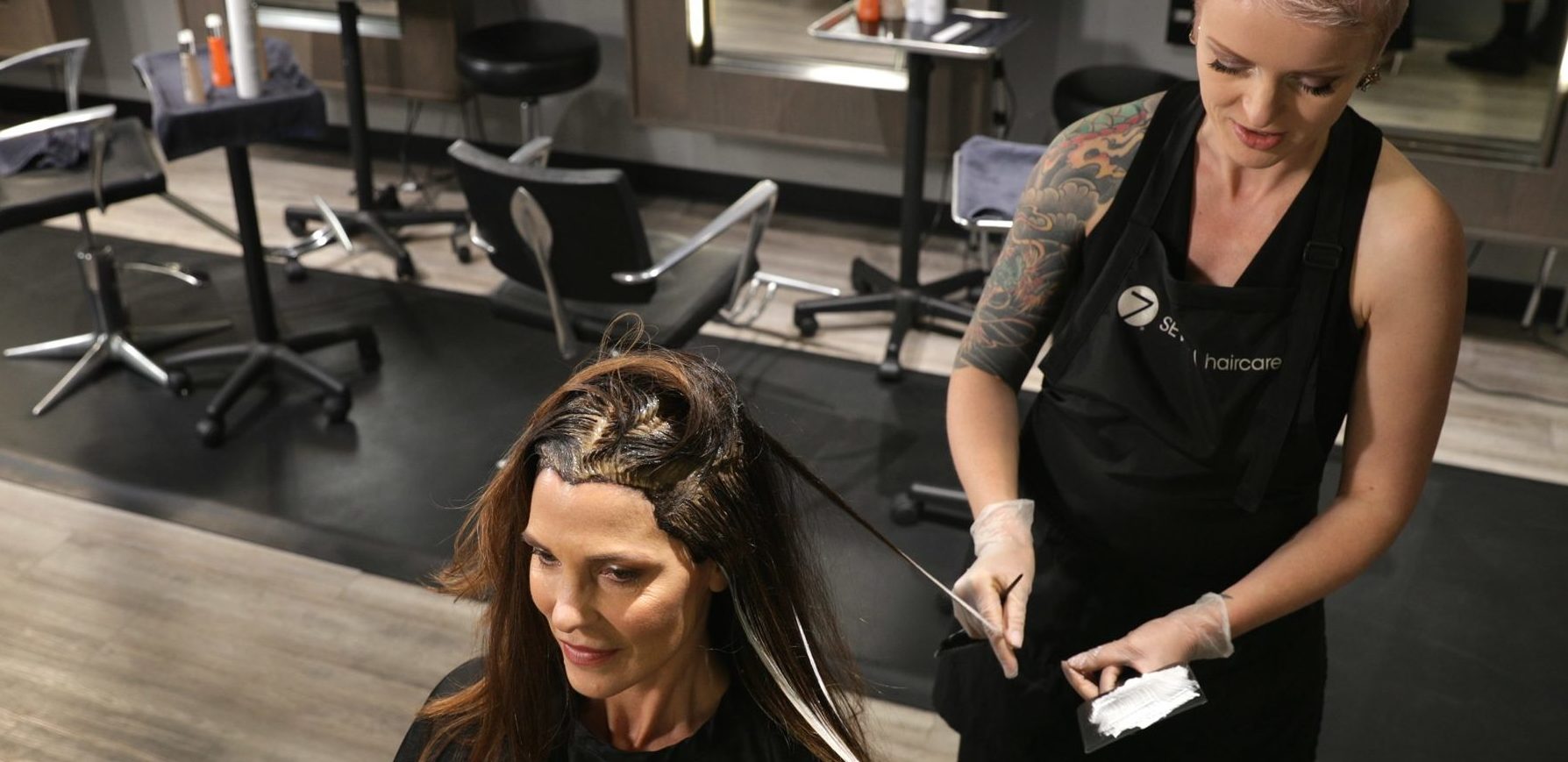 A hairstylist coloring a customer's grey hair in a salon.