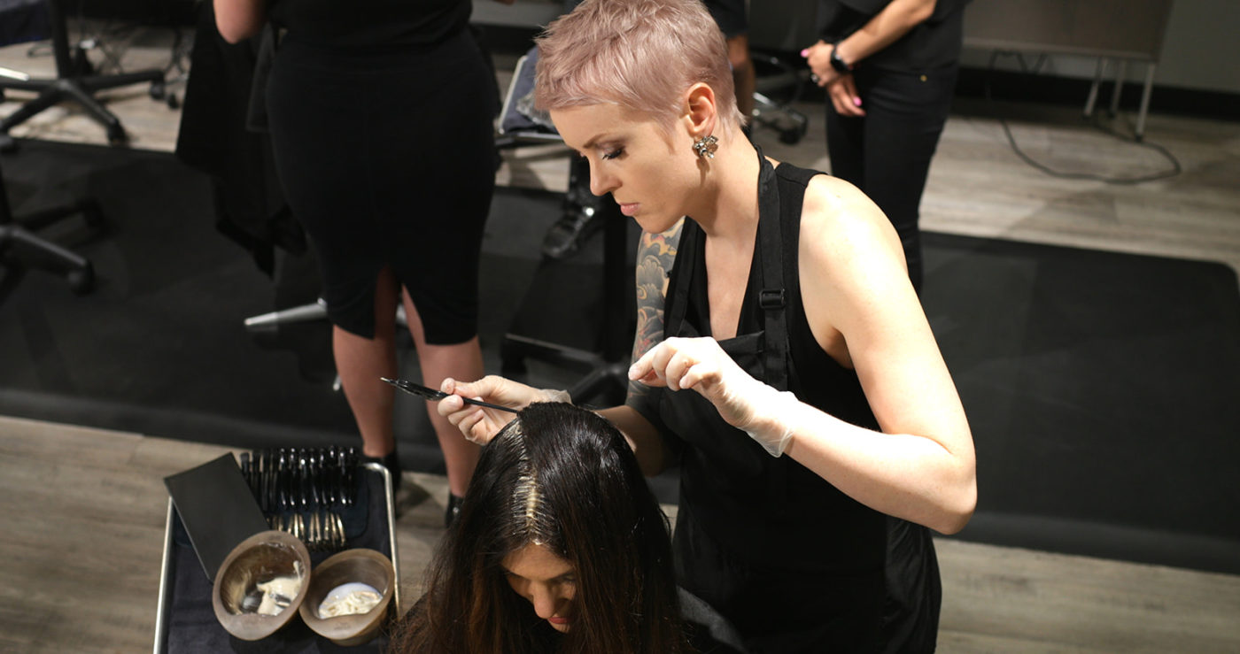 A hairstylist works carefully to color a customer's grey hair.